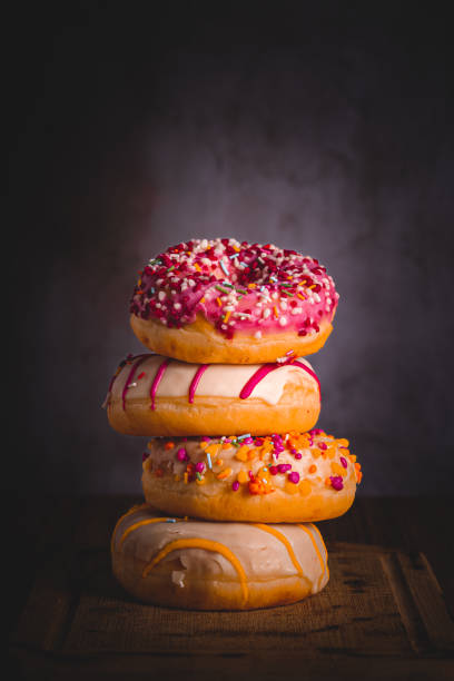 close-up of coloured doughnuts on stacks, with natural light coming in from the right and dark background, copy space