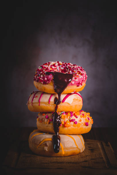 close-up of coloured doughnuts dripping liquid chocolate on them with natural light coming in from the right and dark background, copy space