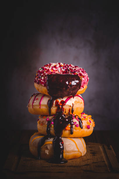 close-up of coloured doughnuts dripping liquid chocolate on them with natural light coming in from the right and dark background, copy spacelibros, flores, oscuro