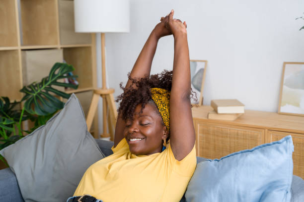 istock Young black woman stretching her arms while relaxing on sofa at home 2166355459
