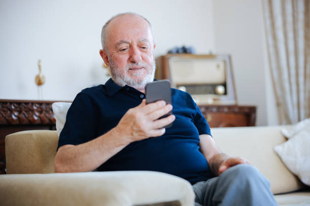 istock Cheerful mature man using mobile phone while relaxing on the sofa at home 2166358364