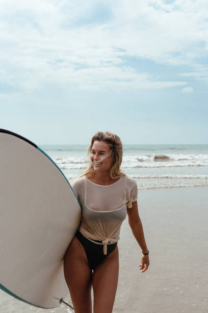 istock Cheerful woman carries a blue surfboard while walking on the beach 2166358593