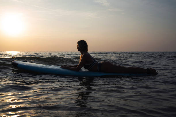 istock Woman Resting on Surfboard in Calm Ocean  During Sunset 2166359394