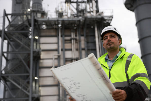 istock System  engineer with glow green safety jacket holds blueprint drawing at Thermal  Power plant power manufacturing site 2166360094