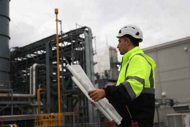 istock System  engineer with glow green safety jacket holds blueprint drawing at Thermal  Power plant power manufacturing site 2166360125
