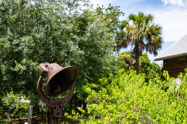 This is a photograph of an old fashioned metal bell with a palm tree in the background on a summer day in Central Florida.