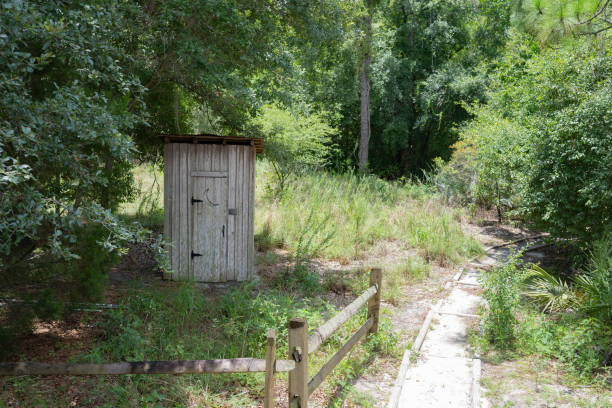 This is a wide angle view of an old fashioned, wooden outhouse by a dirt trail on a summer day in Central Florida.