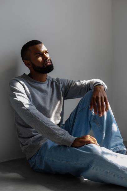 istock African american man sitting in sunlight near grey wall 2166362984