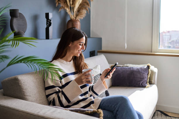 istock Woman relaxing on sofa, enjoying coffee and using smartphone at home 2166365526