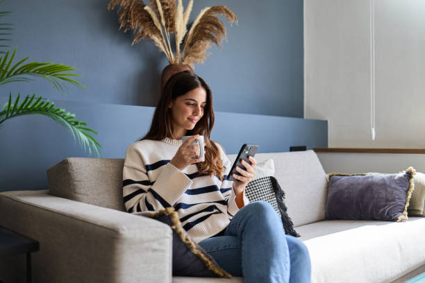 istock Beautiful woman relaxing on sofa using smartphone and drinking coffee at home 2166365648
