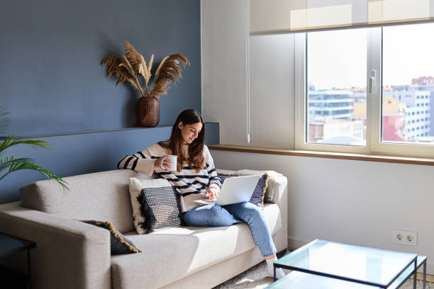 istock Beautiful woman sitting on a comfortable sofa, working remotely on a laptop while enjoying a cup of coffee in her modern apartment 2166365850