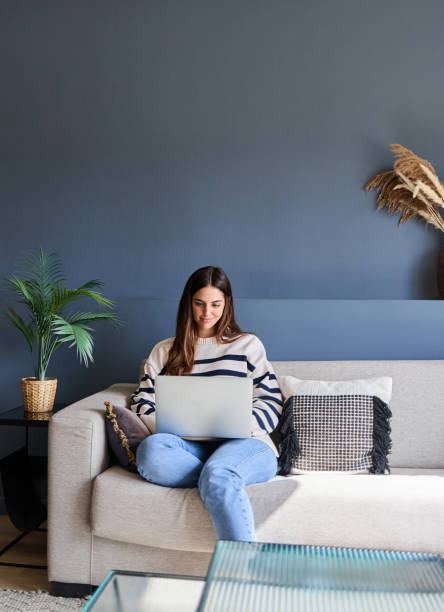 Beautiful woman sitting on a comfortable sofa using a laptop and drinking coffee in a modern living room