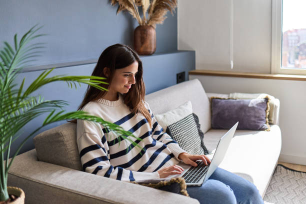 istock Beautiful woman sitting on sofa using laptop at home 2166365903