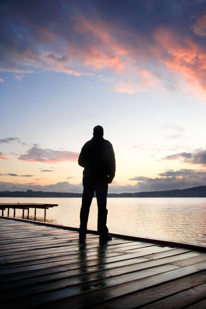 istock Rear view single man on wooden dock looking at seascape view during sunrise 2166369632