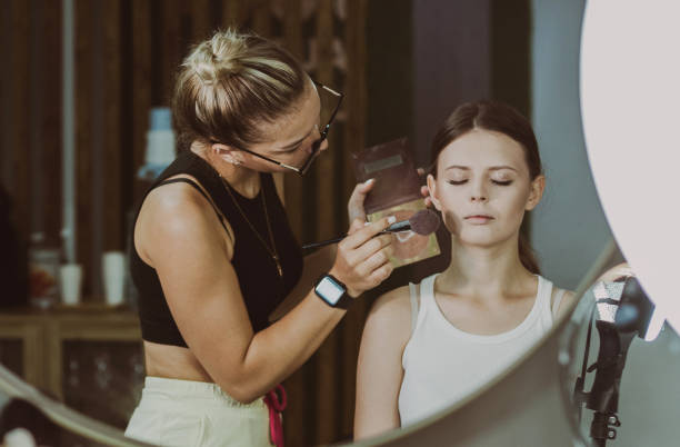 istock A young makeup artist looks at a girl doing makeup. 2166380145