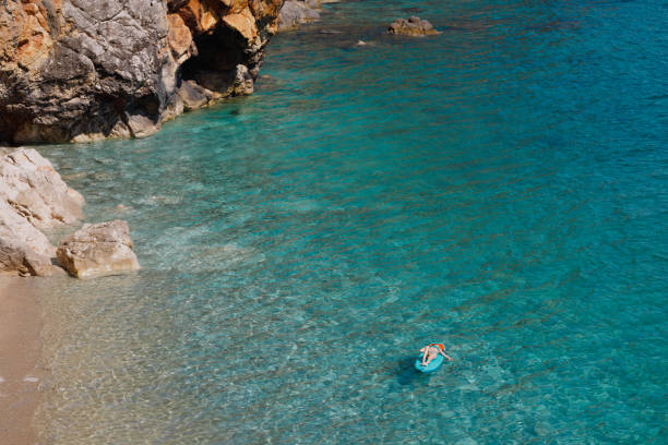 A teenage girl is having fun on the paddleboard surrounded with rocky coast.