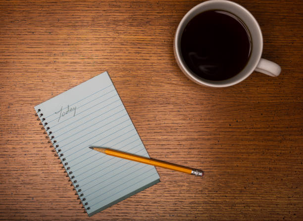 White coffee cup on wooden counter with black coffee and note pad showing start of today list