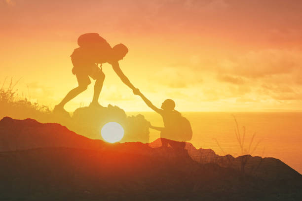 istock People climbing up mountain together giving a helping hand working as a team. 2166389834