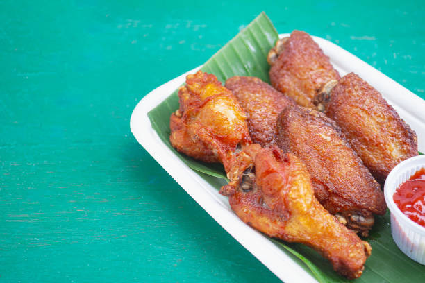 Golden fried chicken wings served with a flavorful dipping sauce on a biodegradable tray with a green leaf. Ideal for topics on finger foods, eco-friendly dining, and tasty snacks.