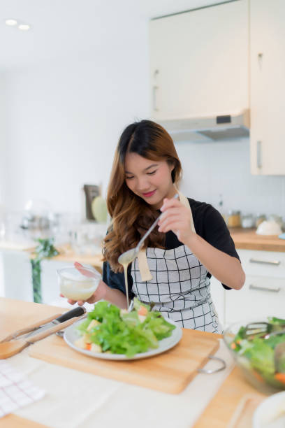 istock Young asian woman use spoon to adding mayonnaise into salad on plate while preparing fresh vegetables salad in bowl and cooking healthy breakfast food in modern kitchen with healthy lifestyle at home 2166399044