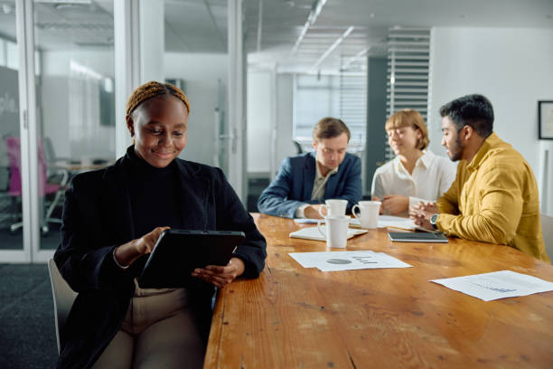 istock Four young multiracial adults in businesswear sitting at conference table using digital tablet at office 2166401222