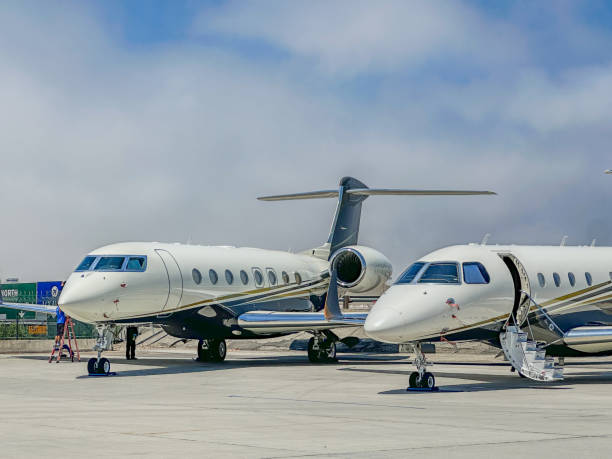 Private Jets Parked Side by Side at the Airport 2 White Blue and Gold Private Jets Parked on a Runway. private jet plane stock pictures, royalty-free photos & images