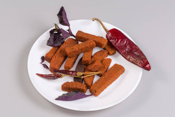 Spicy savory hard rusks made of brown bread among the pods of different dried hot pepper and leaves of fresh purple basil on dish on a gray background