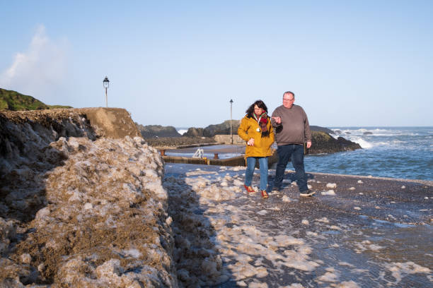 Ballintoy, UK - February 21st, 2022: Frothy foam produced by recent storm and high winds line the walls of Ballintoy Harbour in Co. Antrim, Northern Ireland. The picturesque area on the famous Causeway Coast was used in the filming of TV series Game of Thrones.