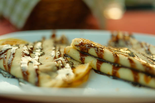 Pancakes covered with chocolate cream on a white plate. The plate is on a red table.