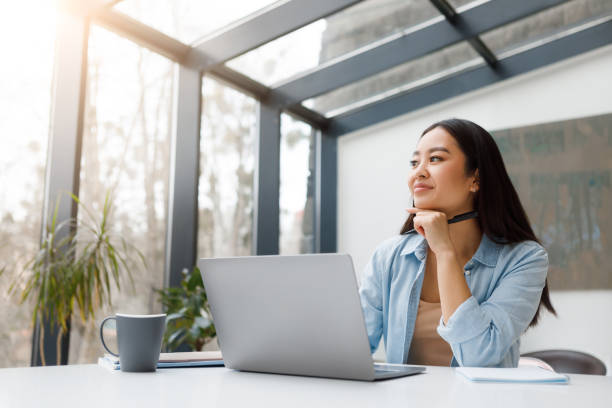 istock Thoughtful asian woman with laptop in sunny workspace 2166428498