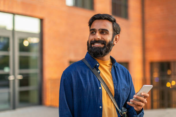 istock Smiling Man Holding Smartphone Outside Brick Building in Evening Light 2166431101