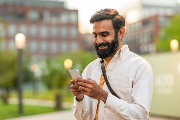 istock Man Smiling While Using Smartphone in Urban Park at Sunset 2166431199