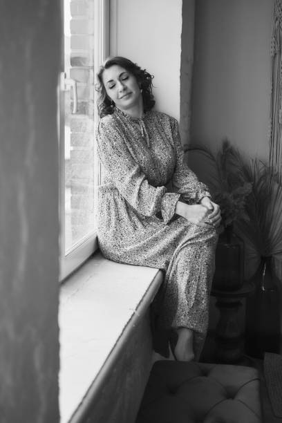 istock a dreamy middle-aged woman by the window 2166431414