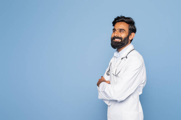 istock Doctor in White Coat Smiling While Standing Against Blue Background 2166431954