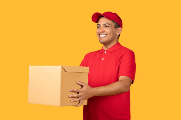 istock Smiling Delivery Person Holding a Package Against Yellow Studio Background 2166440968