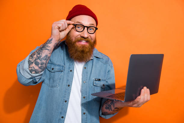 istock Photo of cheerful positive guy dressed denim jacket eyeglasses texting modern device empty space isolated orange color background 2166442962