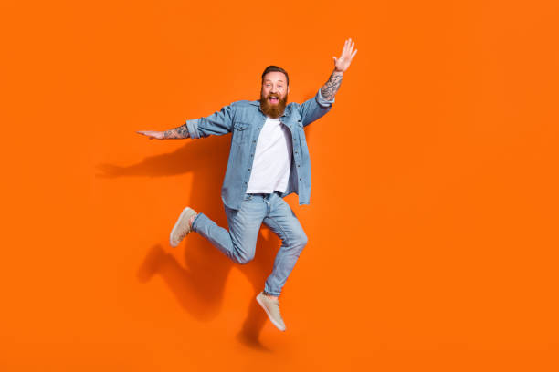 istock Full length photo of cheerful funky guy dressed denim jacket jumping high empty space isolated orange color background 2166443233
