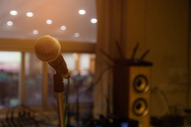 Microphone on stand in professional sound control room. Microphone on stand behind is the console of the sound mixer.