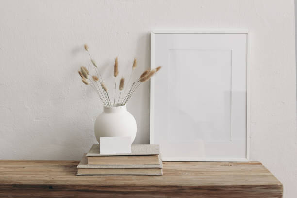 istock Neutral modern interior still life.Vertical white picture frame mockup on wooden table, bench. Ceramic vase with dry Lagurus ovatus grass. Blank business card, old books. White wall background. 2166446631