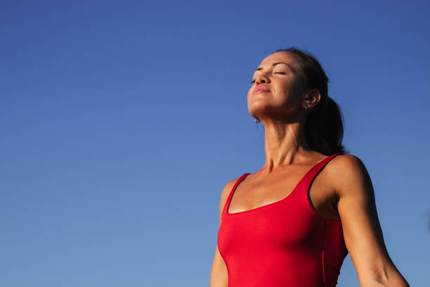 a beautiful woman stands facing the sun.  Young woman looking at sunny blue sky