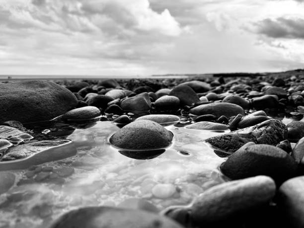 istock Clouds reflecting in a rock pool with rocks and pebbles as far as the eye can see in Northumberland 2166454130