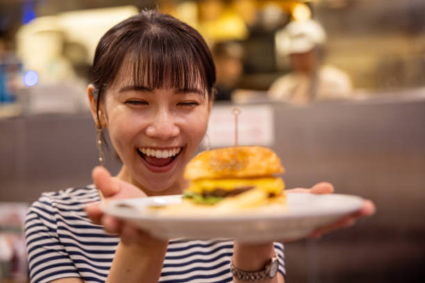 Happy young woman holding hamburger in restaurant