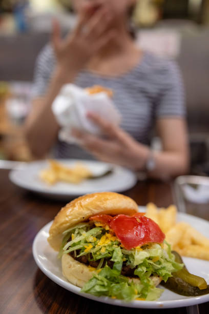Young woman eating hamburger - focus on the hamburger at the front