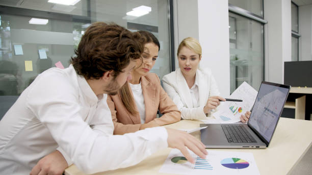 istock Business team in a modern office using a laptop for financial analysis. They brainstorm and discuss a corporate project, collaborating on solutions. Perfect for teamwork and financial strategy themes. 2166461455