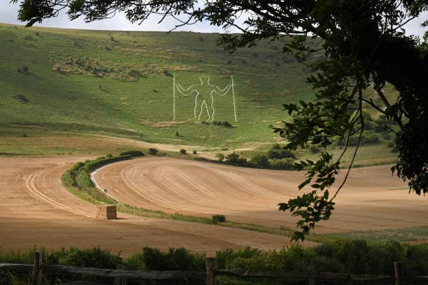 The Long Man of Wilmington, an ancient chalk giant on the South Downs of East Sussex. Newly harvested wheat field beneath and straw bales