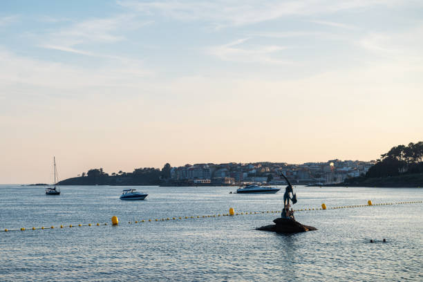 Silhouettes of bathers and small boats moored on Silgar beach in Sanxenxo on a hot summer day in the Rias Baixas in Galicia, Spain.