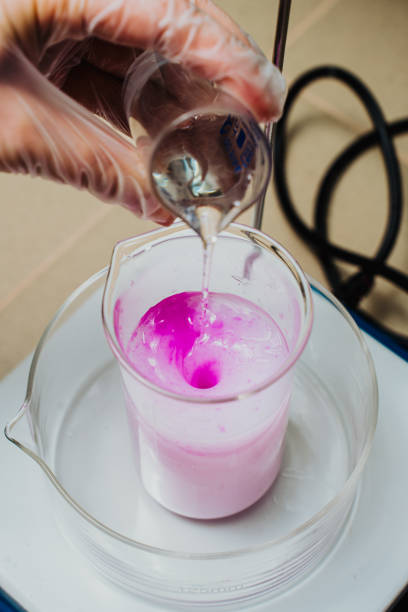 The process of mixing solutions: adding liquid to the pink solution in the laboratory. Medical research. Laboratory studies. Close-up of a measuring cup with liquid