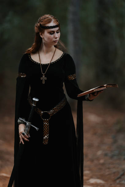 istock Red-haired medieval fantasy queen standing in a forest embodying both strength and wisdom with a book and a sword in her hands 2166474397