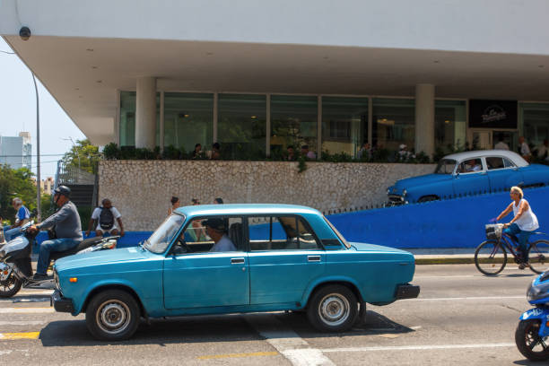 Havana, Cuba - July 29, 2024: Cuban people are out and about by the Hotel Habana Libre (former Hilton) in the downtown district. A Lada car drives in La Rampa, El Vedado