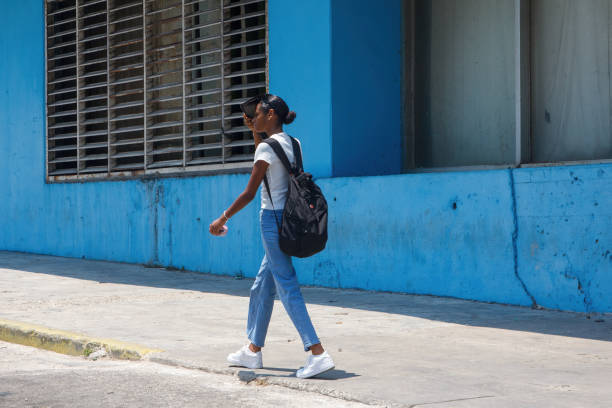 Havana, Cuba - July 29, 2024: A young Cuban woman walks by a weathered wall of a building exterior. Lifestyle of real Cuban people in their daily lifes.
